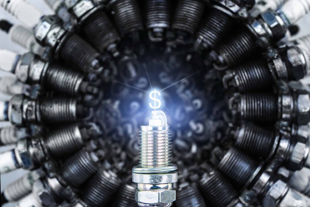 A new spark plug shines in front of old, worn-out spark plugs arranged in a circle.
