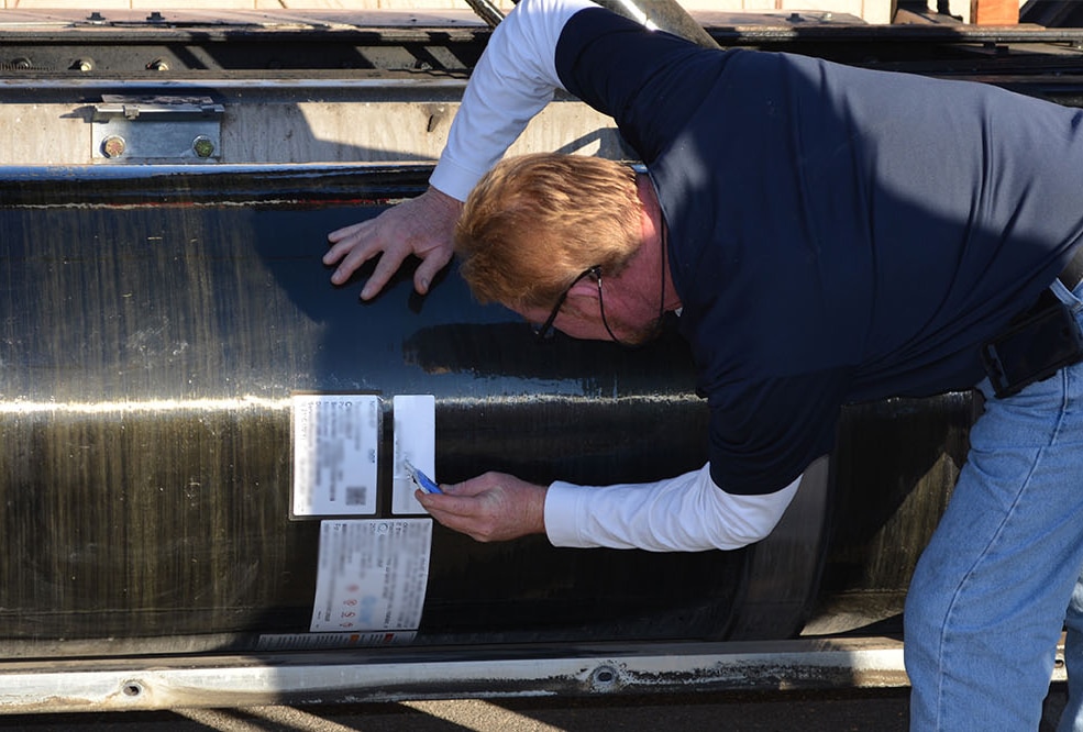 A technician leans over to inspect the cylinder on a natural gas vehicle.